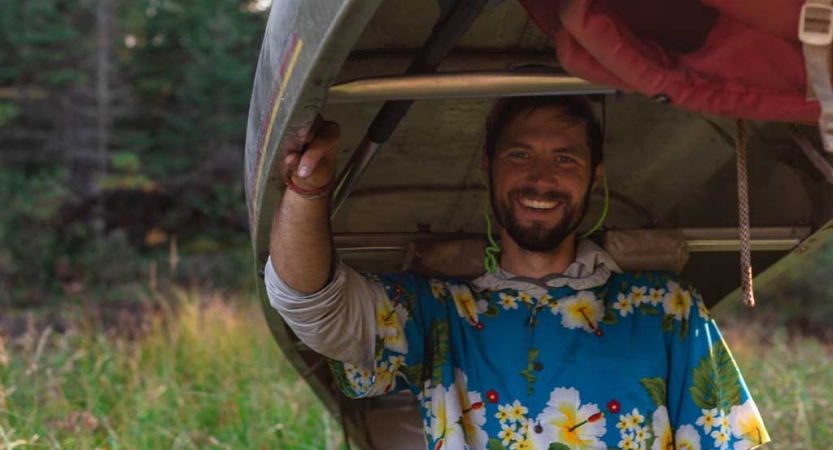 A person smiles while carrying a canoe on their shoulders 